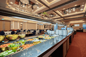 Ontbijtbuffet met een ruime selectie van vers fruit, groenten en salades in een elegant restaurant met gedekte tafels en sfeervolle verlichting.