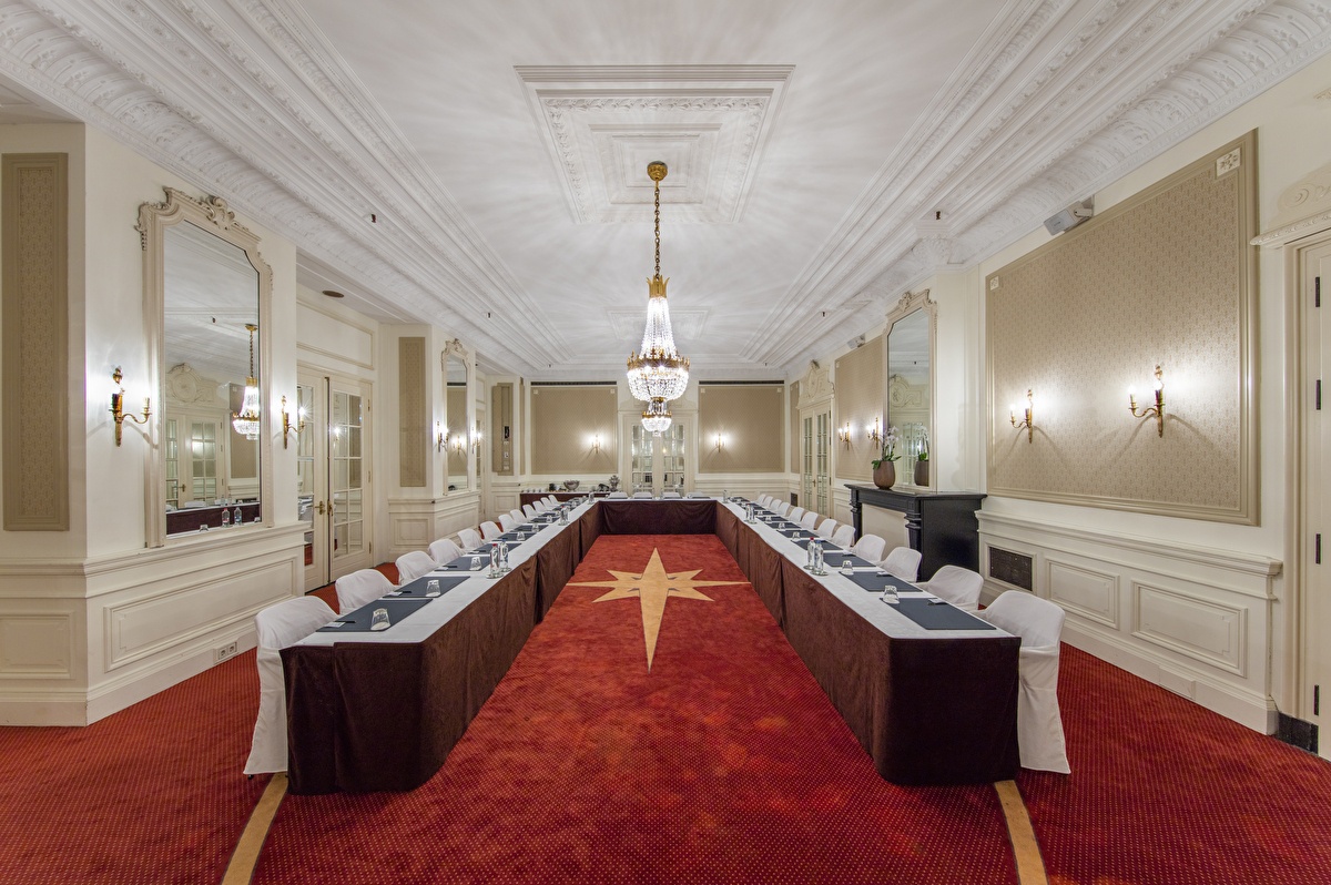 Mirror Room in Grand Hotel Amrâth Kurhaus. The walls are adorned with classic mirrors, red carpeting, and chairs with white slipcovers.