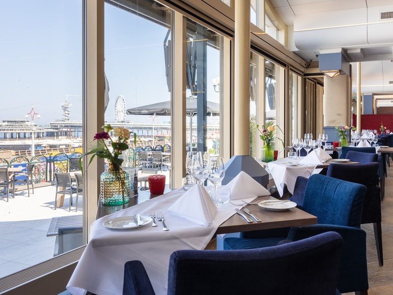 Restaurant Waves met glazen wanden en uitzicht op de pier. De tafels zijn gedekt met servetten, glazen en kaarsen