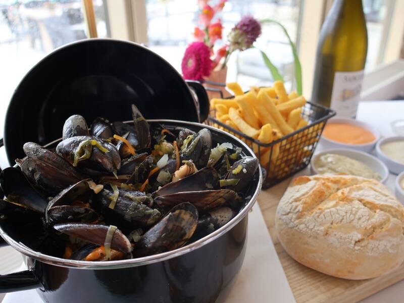Geserveerde pan met verse mosselen in een zwarte pan, drie sausjes, friet, salade en een glas witte wijn (La Guirlande Sauvignon Blanc) op een donkerhouten tafel bij Amrâth Hotels.