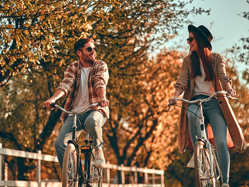 Man and woman are cycling, laughing side by side on a sunny autumn day.