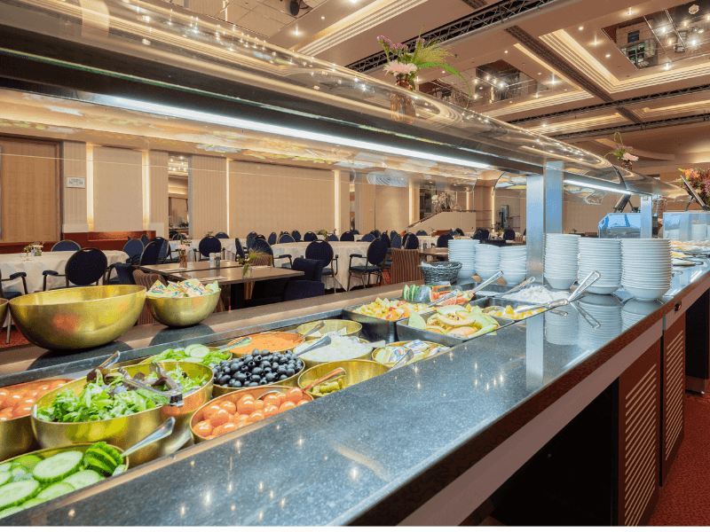Ein Frühstücksbuffet mit verschiedenen Gerichten, Obst und Gemüse, serviert auf weißen Tellern auf einem gedeckten Tisch mit weißen Tüchern.