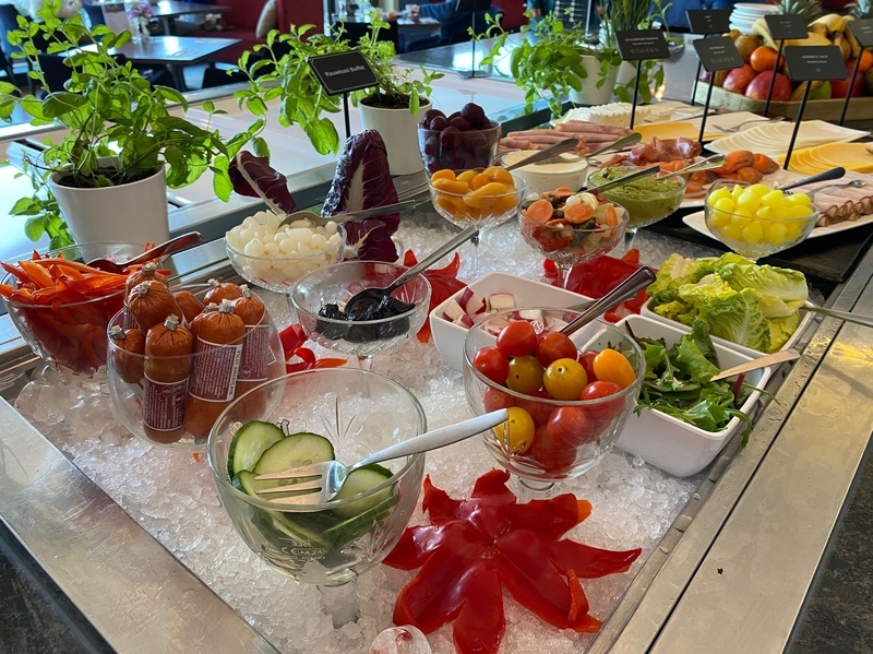 Een ontbijtbuffet met diverse gerechten, fruit en groenten, geserveerd op witte borden op een gedekte tafel met witte lakens.