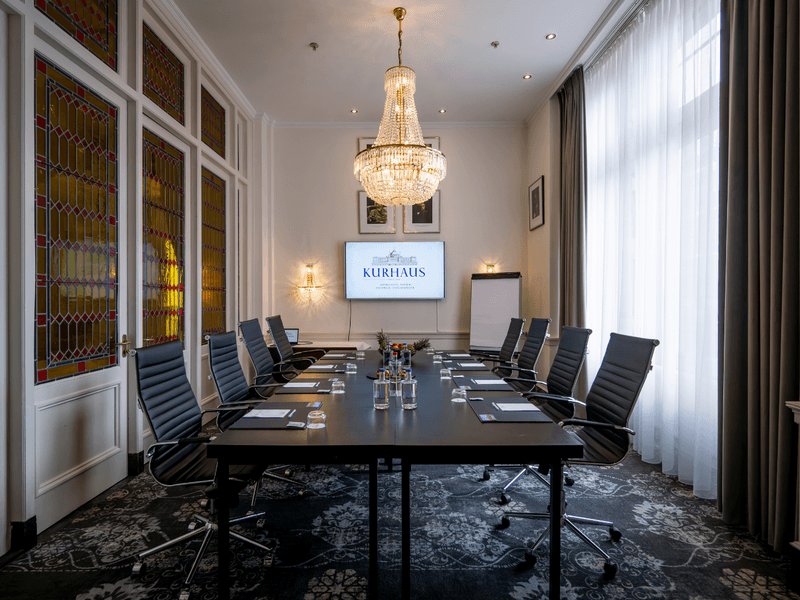 Eleganter Konferenzraum mit runden, weiß gedeckten Tischen, Kristallkronleuchtern und klassischen weißen Wänden mit roten Kunstwerken.