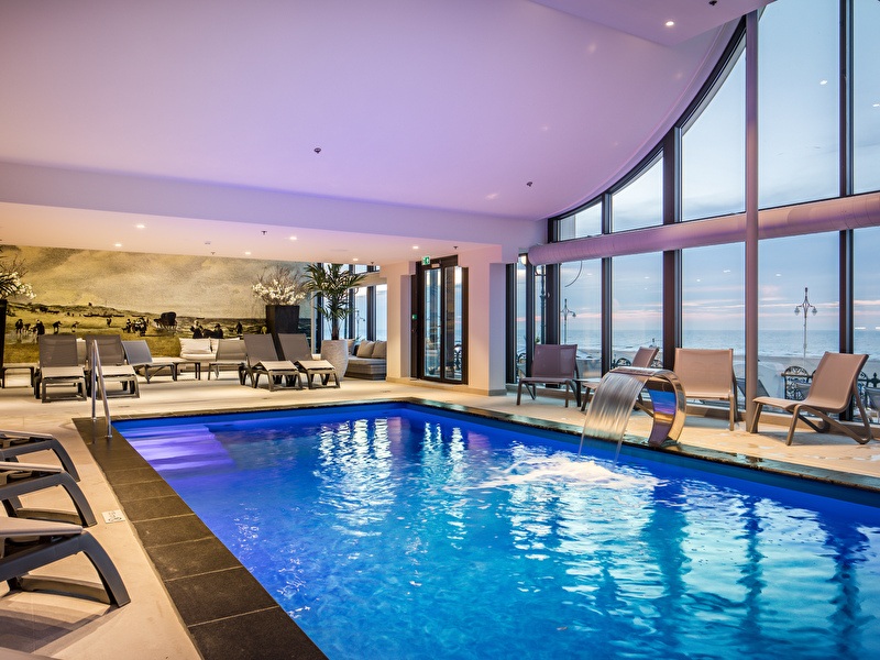 Wellness zwembad met ligbedden langs de rand en uitzicht op de Noordzee